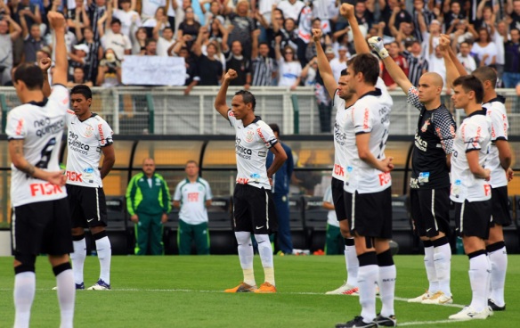 Jogadores do Corinthians antes do início da última partida do Brasileirão 2011 contra o Palmeiras, fazendo gesto característico em homenagem ao Ex-jogador Sócrates, falecido no mesmo dia.